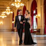 Para w eleganckich strojach wchodzi do klasycznej sali koncertowej z marmurową podłogą i żyrandolami.