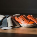Pomarańczowe buty sportowe na drewnianej podłodze obok próbek tkanin o różnych fakturach.